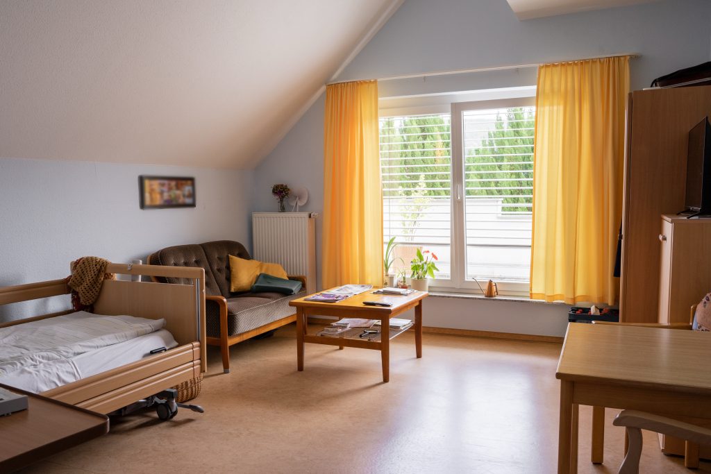 Helles Zimmer mit Pflegebett und Sitzecke